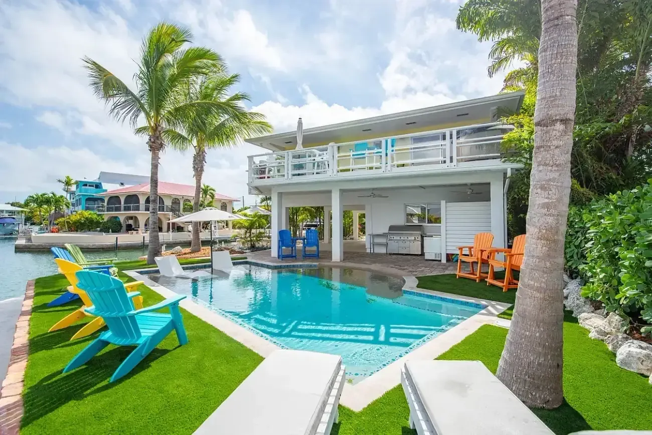 Backyard custom pool with outdoor kitchen, two-story stilt home, colorful seating, and tropical landscaping on the canal