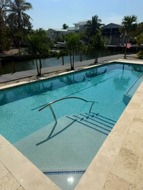 Finished rectangular pool with travertine deck, waterfront canal, and palm trees