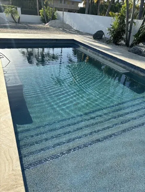 Pool with dark pebble finish, tiled entry steps, and privacy wall