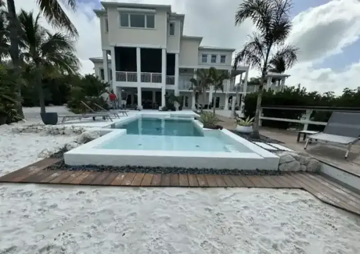 Raised pool with spa, wood deck, beach sand, and coastal stilt home