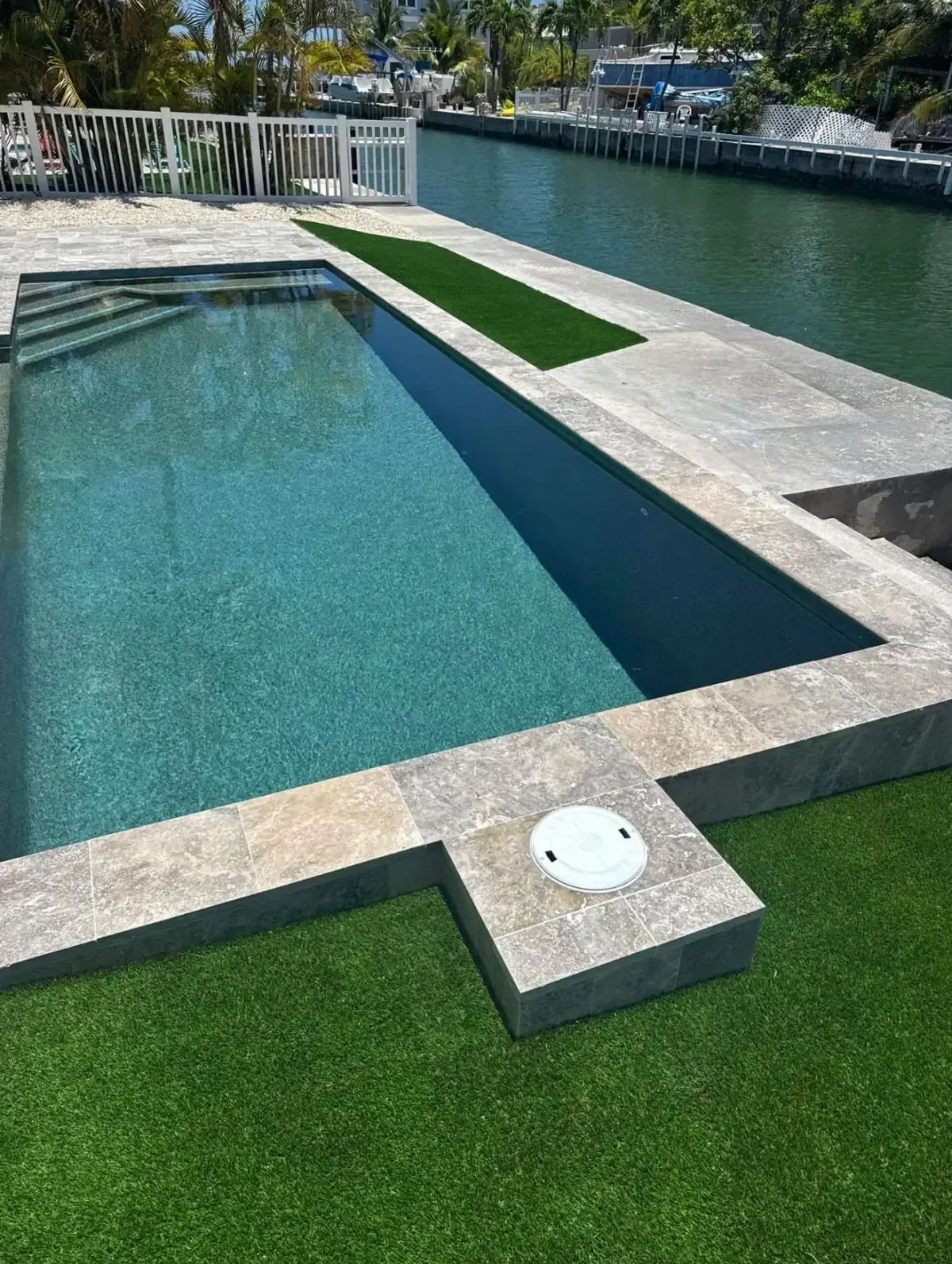 Modern geometric waterfront pool with travertine decking and canal views