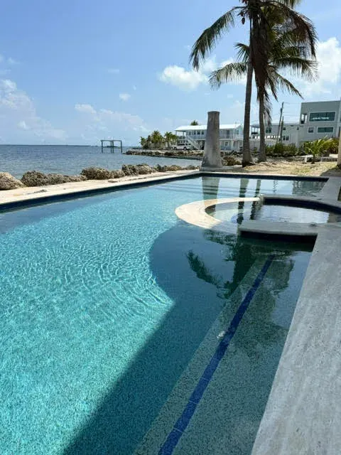 Oceanfront pool with round spa, rock seawall, and palm trees