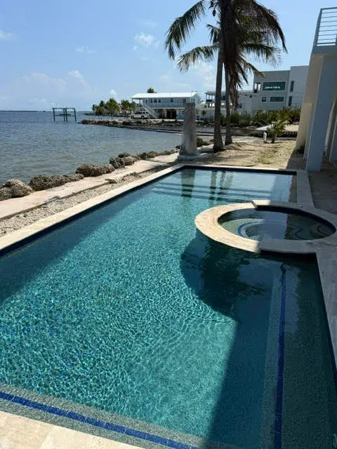 Full-length pool and spa along waterfront with rock seawall and palms
