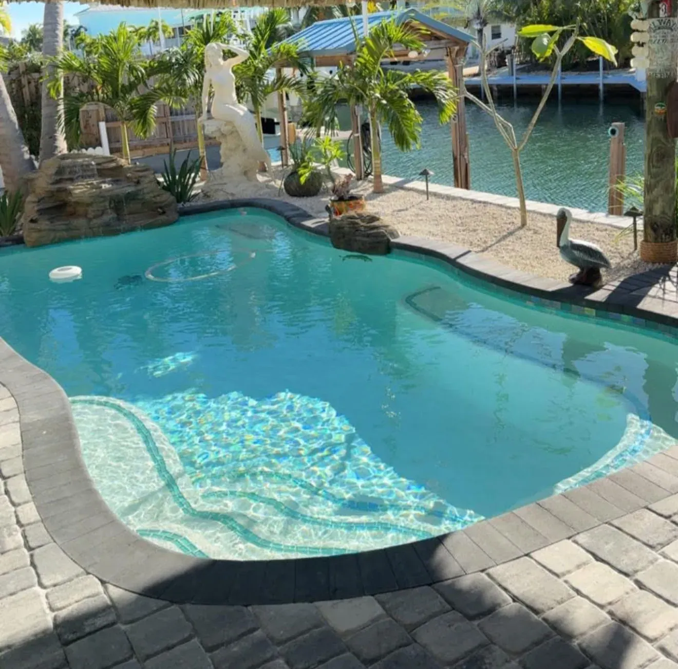 Tropical freeform pool with rock waterfall, tiki hut, and waterfront canal views